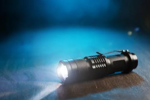 Tactical waterproof flashlight. LED flashlight shines on the table in smoke. Stock Photos