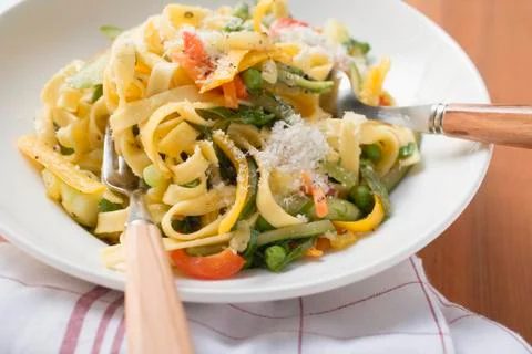 Tagliatelle primavera with vegetables & grated cheese on plate Stock Photos