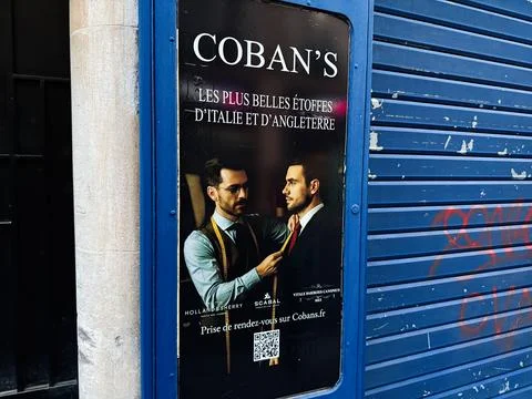 Tailor adjusting client suit and tie on Coban's storefront poster in Paris,.. 스톡 사진
