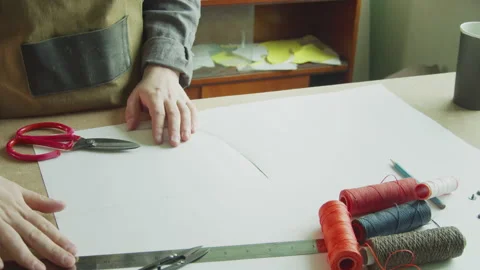 A tailor in an apron cuts out patterns with scissors to create exclusive Stock Footage 143729595