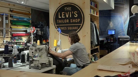 Tailor is customizing jeanswear (adding patches) in Levi's Tailor Shop Stock Footage 109337495