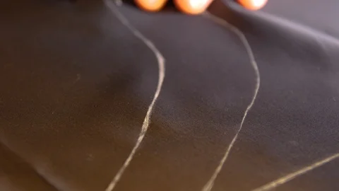 A tailor is cutting lines on a acetate silk lining fabric with his chalk in Stock Footage 127477369
