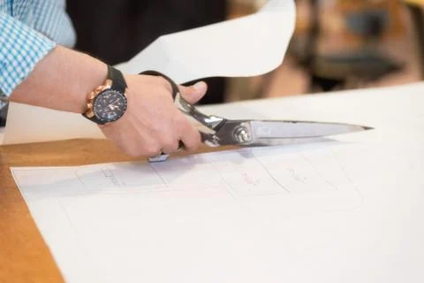 Tailor cutting out the marked pattern on fabric with large scissors on the Stock Photos