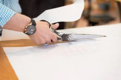 Tailor cutting out the marked pattern on fabric with large scissors on the... Stock Photos