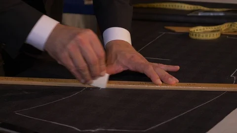 A tailor is drawing lines on a fabric with his chalk in order to make a suit Stock Footage