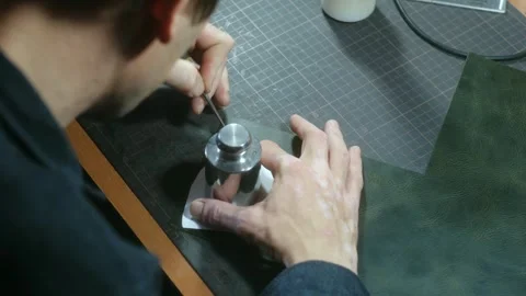 Tailor draws pattern on leather sheet using weight and paper Stock Footage 296748108