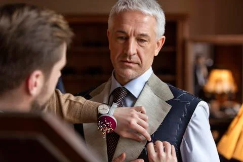 Tailor fitting businessman for suit in menswear shop Stock Photos