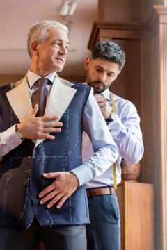 Tailor fitting businessman for suit in menswear shop Stock Photos