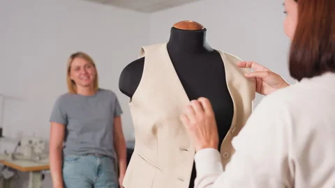 Tailor fitting yellow jacket on mannequin with partner approval in workshop Stock Footage 307137925