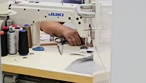 A tailor hands guide fabric through a JUKI sewing machine, with spools 스톡 동영상 312002651