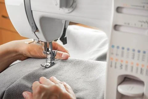 Tailor hands stitching gray fabric on modern sewing machine at workplace in.. Stock Photos