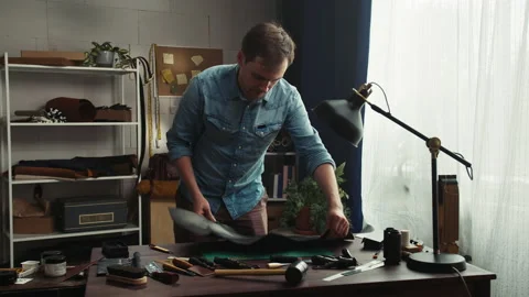 Tailor man putting black leather on workplace, cutting part of material with Stock Footage 157237121