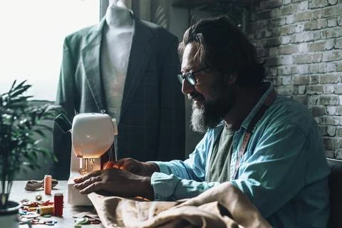 Tailor man working on sewing machine in workshop with dummy wearing suit in.. Stock Photos