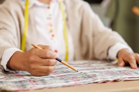 Tailor Marking Checkered Fabric Pattern With Pencil In Sunlit Workshop Close  库存照片