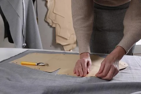 Tailor pinning sewing pattern to fabric at table in atelier, closeup Stock Photos