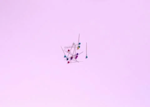 Tailor pins with transparent multi-colored heads lie on a pink background. Stock Photos