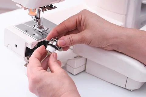 The tailor places the bobbin in the bobbin cap of the sewing machine. Stock Photos