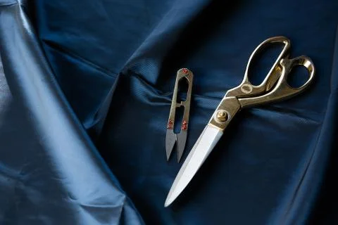 Tailor scissors and clipper for thread lie on a dark blue satin fabric Foto stock