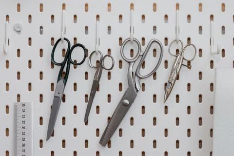 Tailor scissors in different sizes and forms hanging on hooks of perforated w Stock Photos