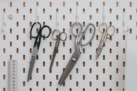 Tailor scissors in different sizes and forms hanging on hooks of perforated w Stock Photos