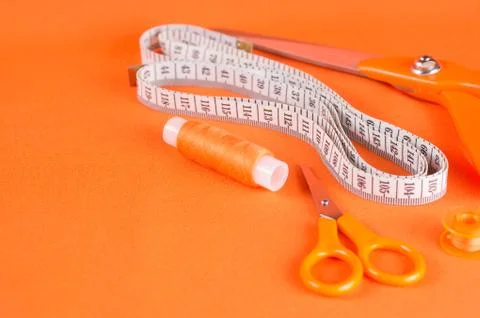 Tailor scissors, inch, centimeter tape, sewing thread on a background of oran Stock Photos