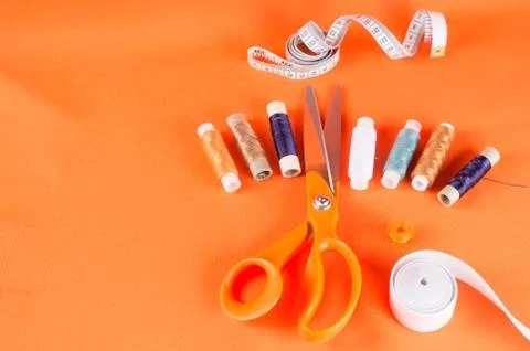 Tailor scissors, inch, centimeter tape, sewing thread on a background of oran Stock Photos