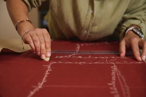 Tailor transfers sewing pattern lines onto red fabric with chalk and a rule.. Stock Photos