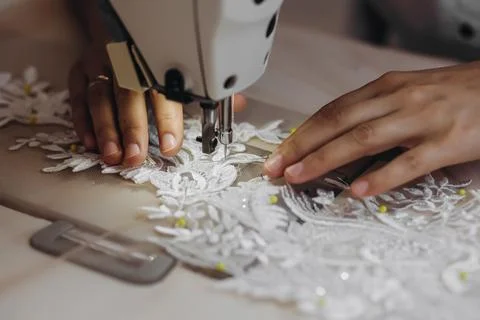 A tailor is using machine for perfecting the white ornament. Stock Photos