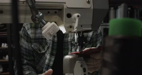 Tailor works on sewing machine in private leather craftshop, making shoes in Stock Footage 200127340