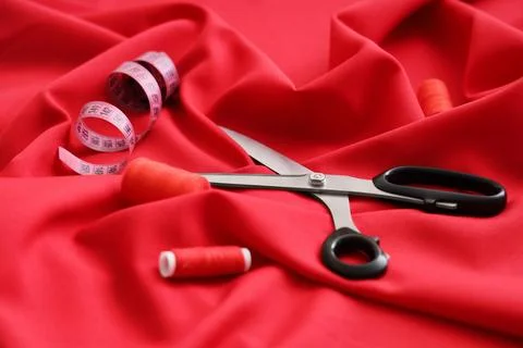 Tailoring and sewing tools with scissors measuring tape and red thread on red Stock Photos
