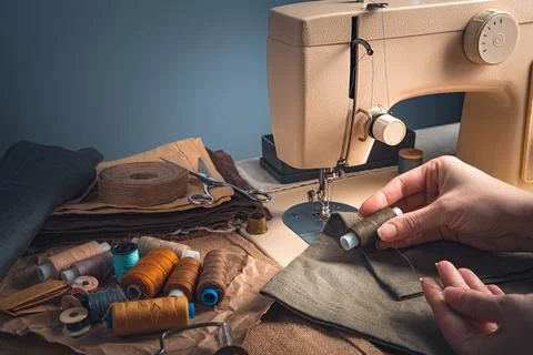 Tailor's hands, thread, fabric and sewing machine on a blue background. Stock Photos