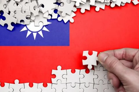 Taiwan flag  is depicted on a table on which the human hand folds a puzzle of Foto stock