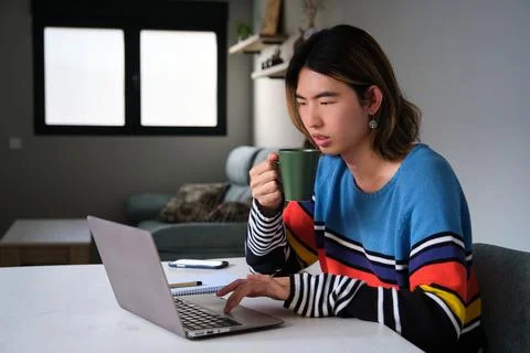 Taiwanese man drinking coffee while working at home with a laptop. Stock Photos