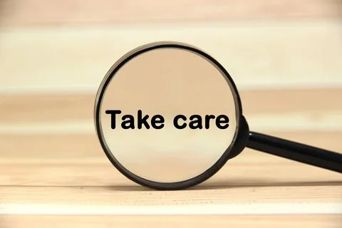 Take care wording  or text on black magnifying glass with wood background.C.. Stock Photos