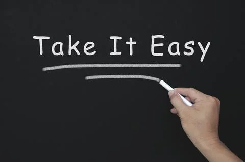 Take it easy text on blackboard with hand holding chalk. Stock Photos