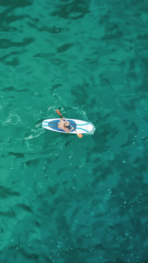 Take a vertical video of someone paddleboarding on clear turquoise water for a Stock Footage 276594577