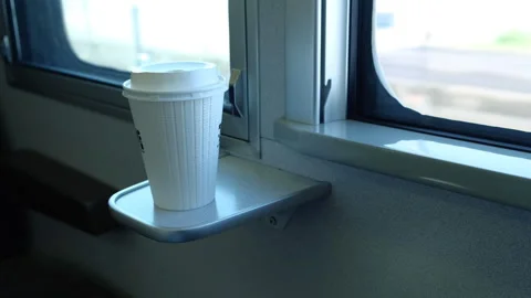 Takeaway coffee cup on a small tray by the window inside a moving train Stock Footage 332226332