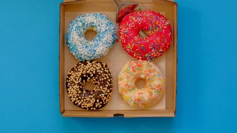 Takes donut from donuts box on blue background. Trendy doughnut assorted. Stock-Footage 118422391