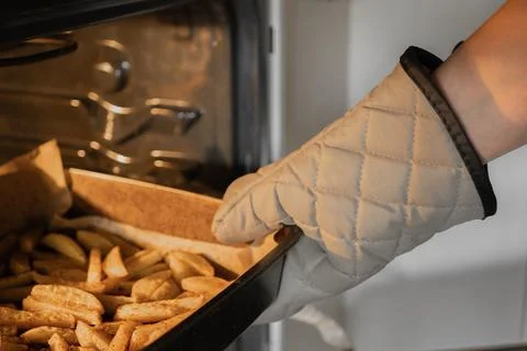 Taking a baking sheet with potato wedges out of the oven Stock Photos