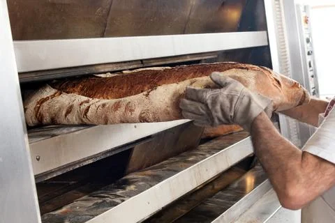Taking big loaf of bread out of oven Foto stock