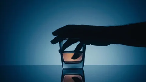 Taking a glass of whiskey on a reflective surface on a blue background Stock Footage 105286319