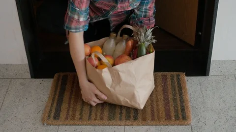 Taking grocery bag with fresh fruits from under the door food delivery Stock Footage 127628702