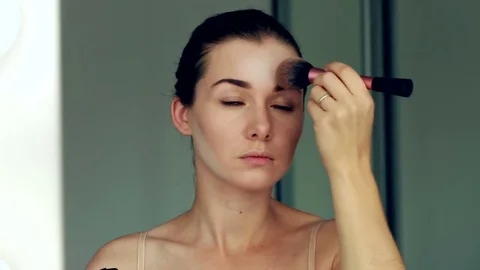 Taking off her make-up. Beautiful cheerful young woman using brush and looking Stock-Footage 80729673