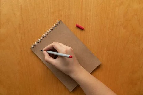 Taking notes in blank craft paper notebook. woman hand and red pencil on wood Stock-Fotos