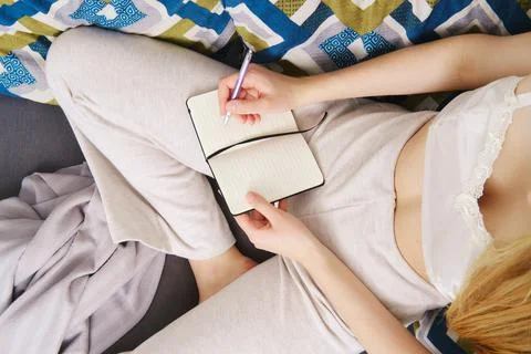 Taking notes in a notebook sitting at home on the couch (view from above) Foto stock