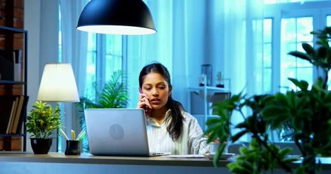 Taking notes on phone call, Indian businesswoman multitasks at desk Stock Footage 342573373