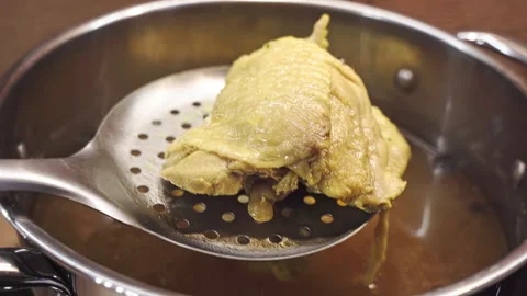 Taking out chicken thigh from a broth onto a wooden cutting board Stock Footage 328649053