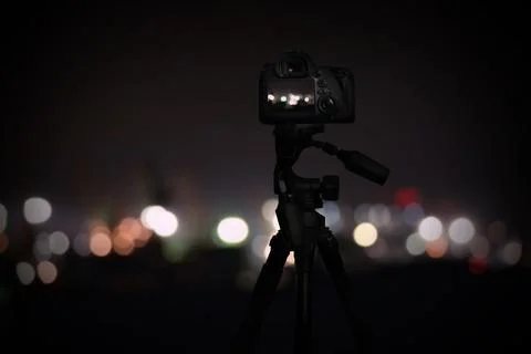 Taking photo of with camera mounted on tripod. Blurred view of city lights at Stock Photos