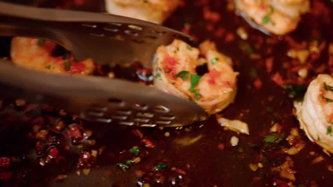 Taking prawns from a pan with a tong and placing them into a serving plate in 4K Stock Footage 138409077
