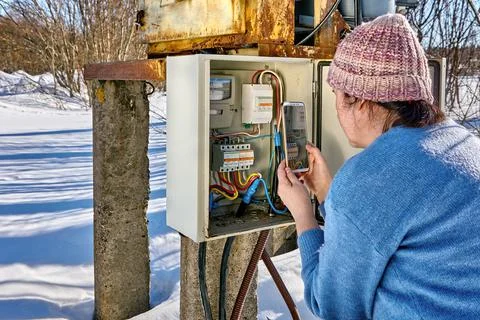 Taking readings from electricity meter using handy by woman in countryside ou Stock Photos